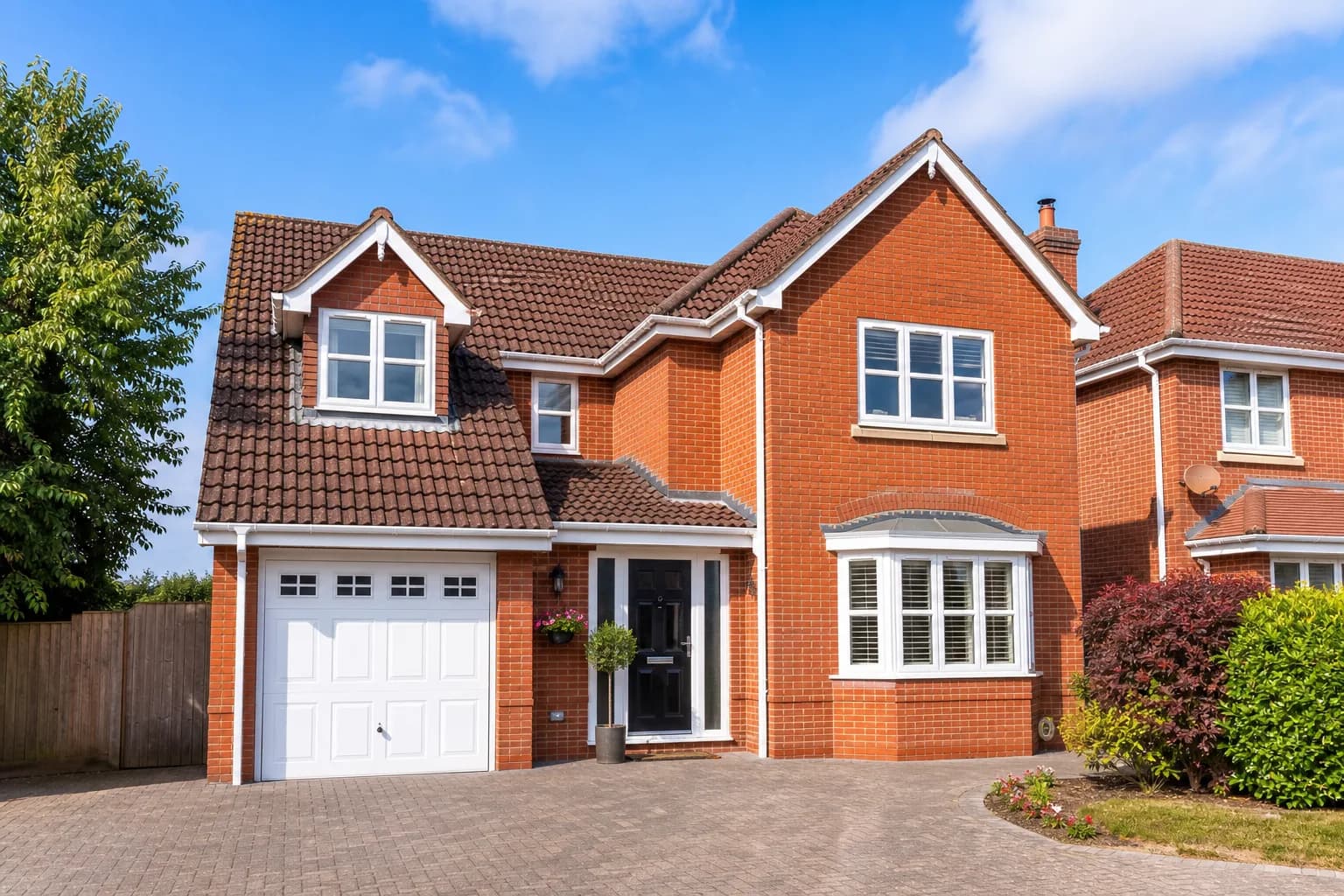 Red-brick UK house with a well-maintained tiled roof and paved driveway